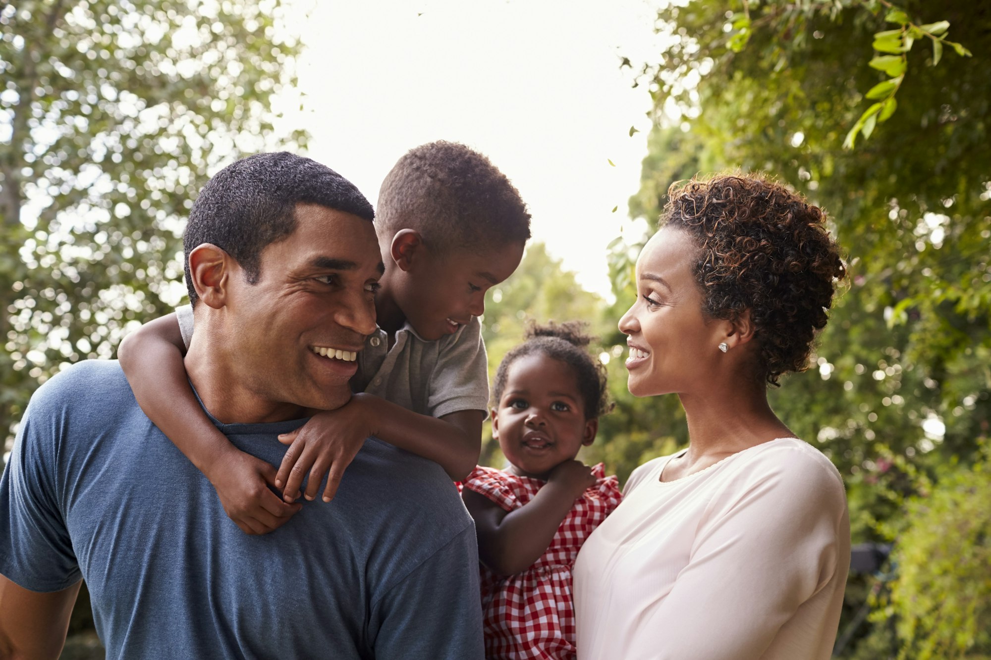 Young African American parents carrying children in garden